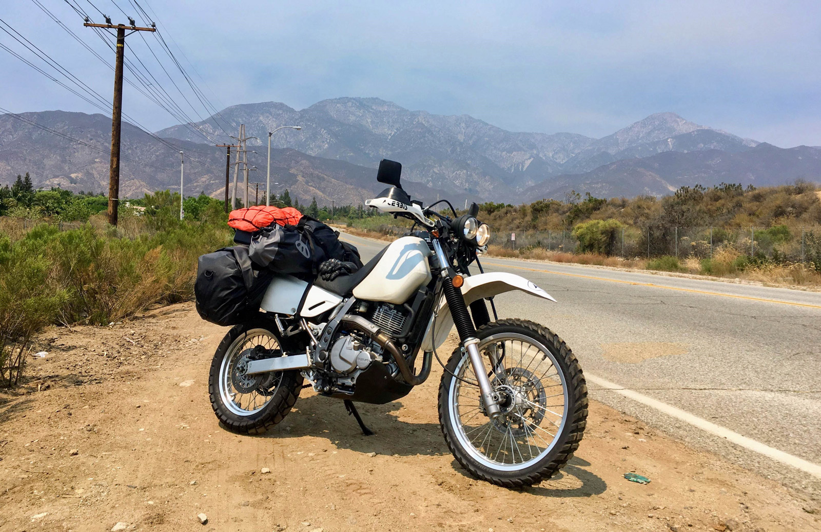 Dylan George Field's fully loaded Suzuki DR650 adventure bike parked in front of the San Gabriel mountains near Los Angeles, California, USA